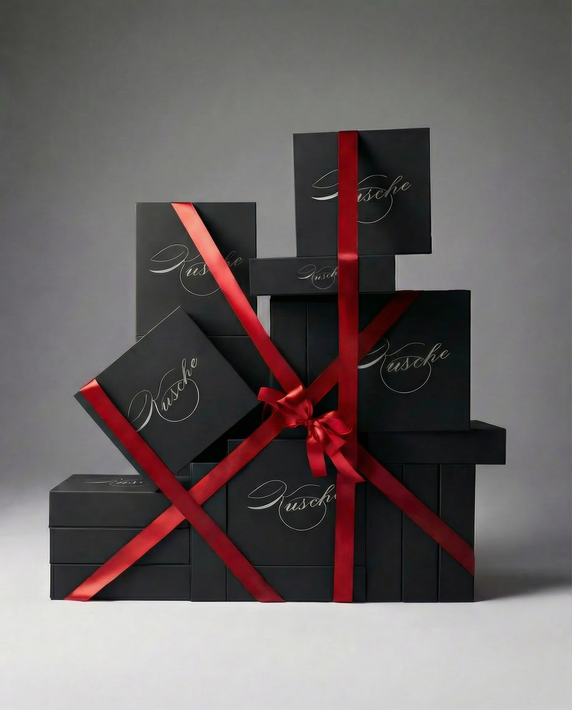 A stacked arrangement of matte-black Kvsche gift boxes with metallic script logos, displayed against a soft grey background in a clean, minimalist composition.